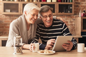 Cheerful Senior Couple Spending Time With Digital Tablet In Kitchen