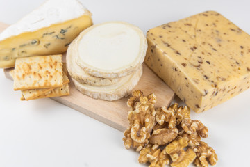 Fresh cheeses of different flavors with nuts on black chalkboard plate and wooden board on white commercial background and space for text