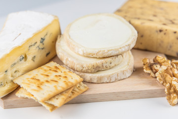 Fresh cheeses of different flavors with nuts on black chalkboard plate and wooden board on white commercial background and space for text