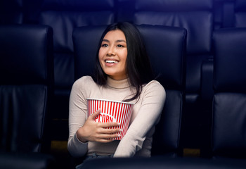 Going to movies alone concept. Pretty Asian woman with popcorn enjoying film in cinema