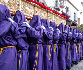 Nazarenos portando un trono de Semana Santa con túnica y capirote de color violeta