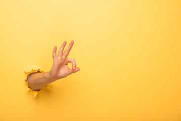 cropped view of man showing ok sign through yellow paper hole - obrazy, fototapety, plakaty