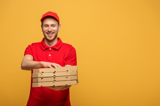 happy delivery man in red uniform giving pizza boxes isolated on yellow - Powered by Adobe