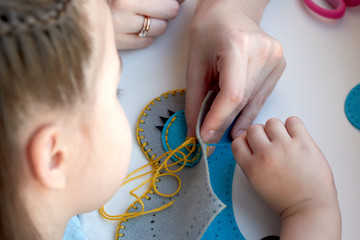 Сhild is sewing a toy owl from felt. Mother teaches the child to sew. 