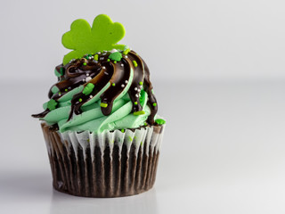 Plakat St. Patrick’s Day cupcakes. A chocolate cupcake decorated with a heaping pile of green frosting with chocolate syrup poured over it and green and white sprinkles with a four leaf clover!
