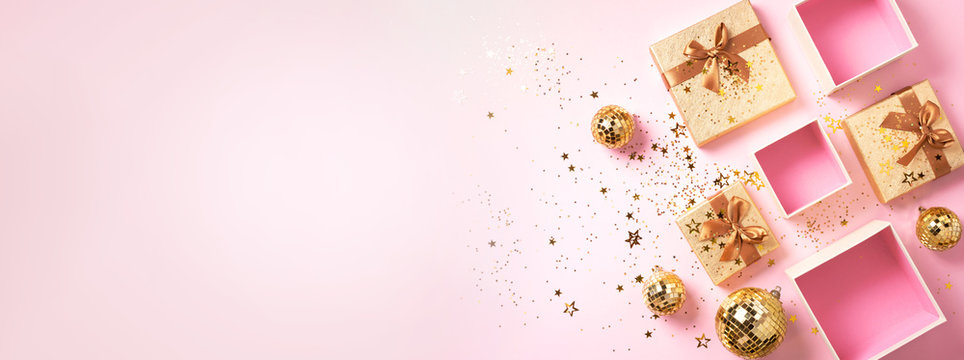 Gift box, shiny gold disco balls, sparkling gold glitter on pink background. New year baubles, star sparkles. New year, Christmas, Valentine's day concept of greetings. Copy text. Top view, flat lay.