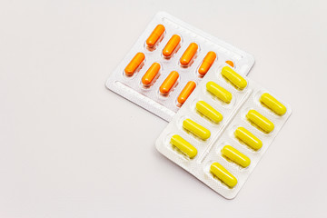 Pharmaceutical tablets, orange and yellow capsules in blister pack isolated on white background