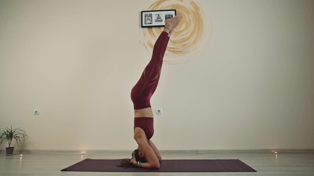 A pretty female yoga instructor demonstrates the bends of the body, stretches, relaxes, stands on her head.