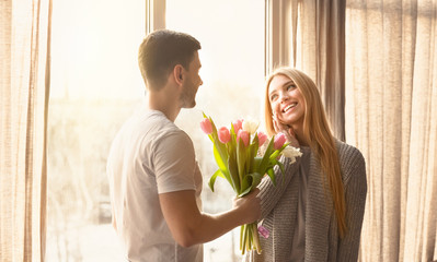 Romantic moment. Young man giving flowers to his wife on special day