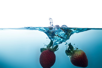 2 strawberries fall into the clear blue water until the sponge splits beautifully on the clear blue background.