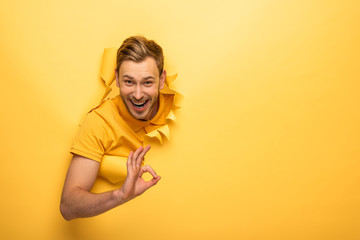 happy handsome man in yellow outfit in yellow paper hole showing ok sign