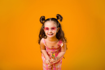 Adorable girl licking lollipop, on yellow background