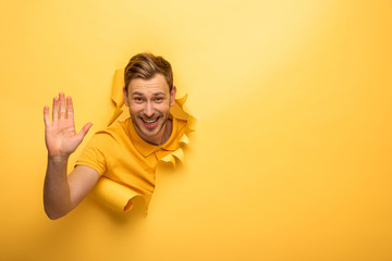 happy handsome man in yellow outfit in yellow paper hole giving high five
