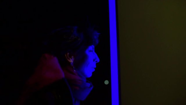 Blue silhouette of a woman looking out of a shop window. Light illuminates the face. City lighting concept.