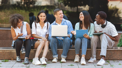 Fototapeta premium Joyful University Students Sitting At Campus With Laptop And Laughing Together