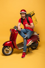 happy delivery man with backpack on scooter showing thumb up on yellow background © LIGHTFIELD STUDIOS
