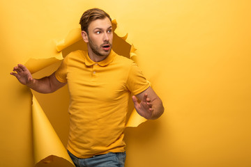 surprised handsome man in yellow outfit walking through yellow paper hole