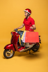 smiling delivery man in red uniform with shopping bags on scooter on yellow background