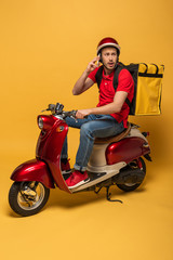 worried delivery man with backpack on scooter talking on smartphone on yellow background