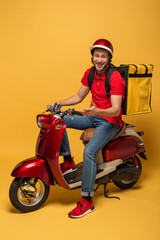 happy delivery man with backpack on scooter on yellow background © LIGHTFIELD STUDIOS