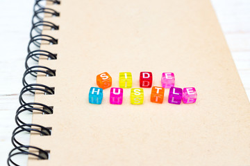 Side Hustle words made form multicolored square beads on spiral notebook cover. Concept image of passive income