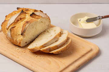 Cut round bread, loaf or Boule on wood cutting board. Near there is plate with butter and knife. Grey background. Concept: healthy food, breakfast. 