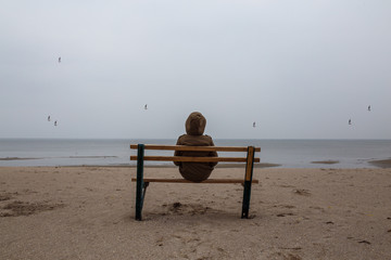 Naklejka na ściany i meble Loneliness human sitting on a bench at the seashore. Foggy morning at sea.