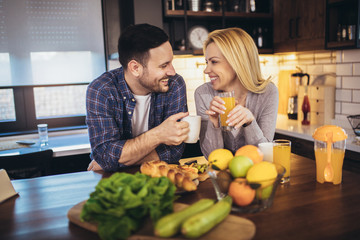 Beautiful young couple is talking and smiling while cooking healthy food in kitchen at home.