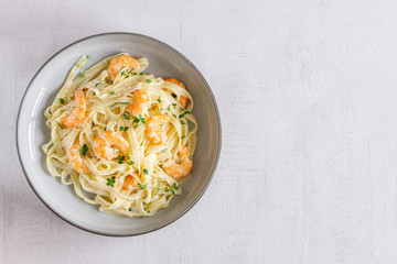 Italian pasta Tagliatelle in a creamy sauce with shrimp and persil on a plate, top view. Isolated. Copy space. Grey background. Concept: healthy food, tasty dinner. Top view. 