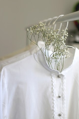 Collection of white shirts and blouses and gypsophila flowers on a clothing rack. Selective focus.