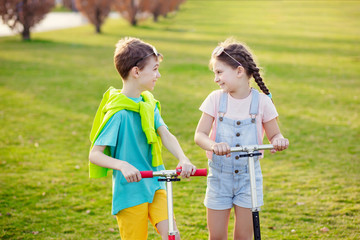 Fototapeta premium Portrait of two little happy children with scooters. Doing outdoor sports in the park.
