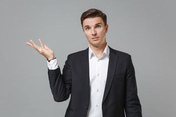 Bewildered young business man in classic black suit shirt posing isolated on grey wall background studio portrait. Achievement career wealth business concept. Mock up copy space. Pointing hand aside.