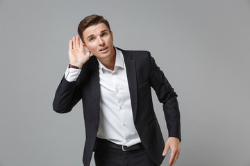 Curious young business man in classic black suit shirt posing isolated on grey background in...