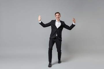 Fototapeta na wymiar Cheerful laughing young business man in classic black suit shirt posing isolated on grey background studio portrait. Achievement career wealth business concept. Mock up copy space. Spreading hands.