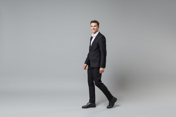 Side view of smiling young business man in classic black suit shirt posing isolated on grey wall background in studio. Achievement career wealth business concept. Mock up copy space. Looking camera.