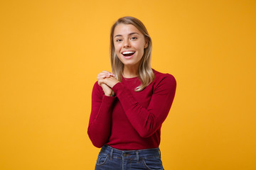 Cheerful young blonde woman girl in casual clothes posing isolated on yellow orange background studio portrait. People sincere emotions lifestyle concept. Mock up copy space. Holding hands folded.
