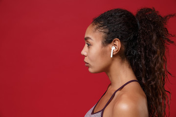 Naklejka na ściany i meble Side view of young african american sports fitness woman in sportswear working out isolated on red background studio portrait. Sport exercises healthy lifestyle concept. Listen music with earpods.