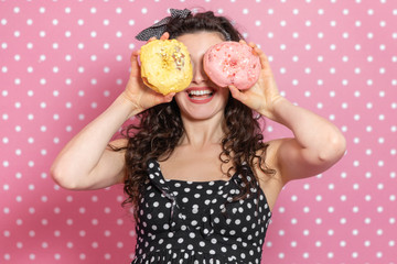 Glad young lady is looking through two doughnuts like through binocular and smiling pleasantly.