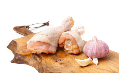 Raw uncooked chicken legs with garlic, drumsticks on wooden board.