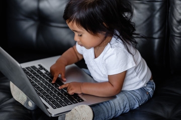 Side view of talented little mixed race girl pushing button on laptop while looking at cartoons...