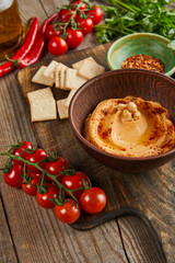 Selective focus of bowls with hummus and spices, ripe vegetables and crackers on wooden background