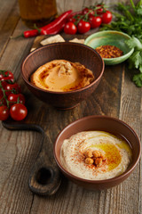 Selective focus of bowls with paprika and hummus, vegetables and parsley on wooden background