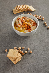 Delicious hummus in bowl with chickpea and crackers on grey background
