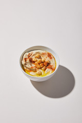 Hummus with chickpea, spices and olive oil in bowl on grey background