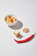 Bowl with tasty hummus near crackers, chili pepper and chickpea on grey background