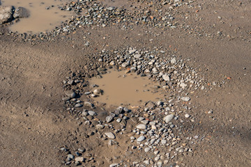 A bumpy wet gravel road after the rain, gravel road is full of potholes