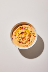 Top view of bowl with delicious hummus on grey background