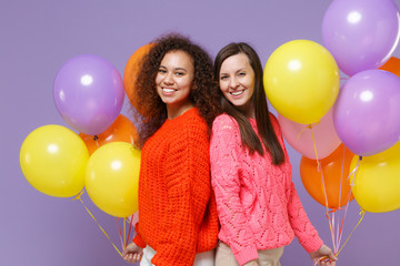 Smiling two european african american women friends in knitted sweaters isolated on violet purple...