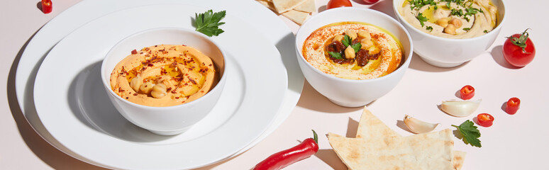 Plates and bowls with hummus, vegetables and pita bread on grey, panoramic shot