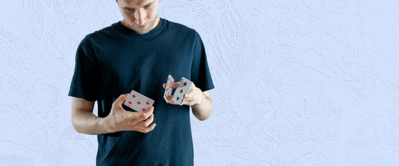 person holding some playing cards and doing the magic trick focus, standing angaist the wall wide...